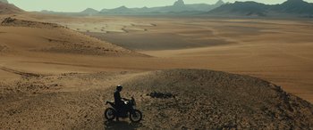 Movie still from “Kandahar” (2023), directed by Ric Roman Waugh – A person on a motorcycle in the middle of the desert; Extreme Wide shot, High angle