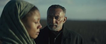 Movie still from “Kandahar” (2023), directed by Ric Roman Waugh – An older man and a younger woman standing next to each other; Close Up shot, Over the shoulder angle