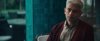 Movie still from “Khufiya” (2023), directed by Vishal Bhardwaj – An older man sitting in a chair in front of a green wall; Close Up shot, Over the shoulder angle