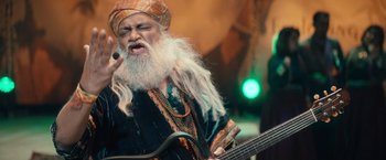 Movie still from “Khufiya” (2023), directed by Vishal Bhardwaj – An old man with a long white beard playing a guitar; Medium shot, Low angle