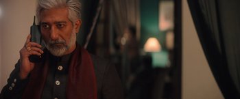 Movie still from “Khufiya” (2023), directed by Vishal Bhardwaj – An older man with a gray beard wearing a red scarf; Close Up shot, Over the shoulder angle