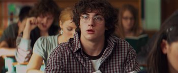 Movie still from “Kick-Ass” (2010), directed by Matthew Vaughn – A young man wearing glasses and a checkered shirt looks at the camera; Close Up shot, Over the shoulder angle