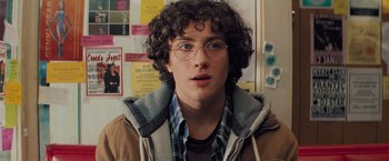 Movie still from “Kick-Ass” (2010), directed by Matthew Vaughn – A young man with curly hair wearing glasses and a plaid shirt; Close Up shot, Over the shoulder angle