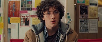 Movie still from “Kick-Ass” (2010), directed by Matthew Vaughn – A young man with curly hair wearing glasses and a plaid shirt; Close Up shot, Over the shoulder angle