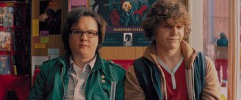 Movie still from “Kick-Ass” (2010), directed by Matthew Vaughn – Two men standing next to each other in front of a poster; Close Up shot, Over the shoulder angle