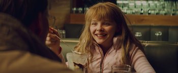 Movie still from “Kick-Ass” (2010), directed by Matthew Vaughn – A young girl smiles while eating a dessert; Close Up shot, Over the shoulder angle