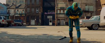 Movie still from “Kick-Ass” (2010), directed by Matthew Vaughn – A person in a blue and yellow suit with a knife in the street; Wide shot, High angle
