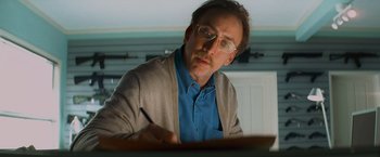Movie still from “Kick-Ass” (2010), directed by Matthew Vaughn – A man with glasses is writing at a desk; Close Up shot, Low angle