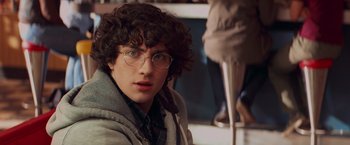 Movie still from “Kick-Ass” (2010), directed by Matthew Vaughn – A young man with curly hair wearing glasses and a jacket; Close Up shot, Over the shoulder angle