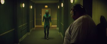 Movie still from “Kick-Ass” (2010), directed by Matthew Vaughn – A man in a green suit is walking down a hallway; Wide shot, Over the shoulder angle