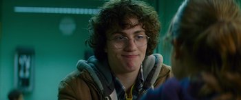 Movie still from “Kick-Ass” (2010), directed by Matthew Vaughn – A man with curly brown hair and glasses is smiling for the camera; Close Up shot, Over the shoulder angle