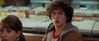 Movie still from “Kick-Ass” (2010), directed by Matthew Vaughn – A man with curly brown hair wearing glasses and a brown jacket; Close Up shot, Over the shoulder angle