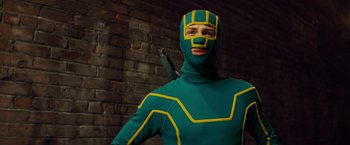 Movie still from “Kick-Ass” (2010), directed by Matthew Vaughn – A man in a green and yellow costume holding a gun; Medium shot, Low angle