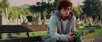 Movie still from “Kick-Ass” (2010), directed by Matthew Vaughn – A man sitting on top of a wooden park bench; Medium shot, Over the shoulder angle