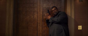 Movie still from “Kick-Ass” (2010), directed by Matthew Vaughn – A man in a suit holding a gun in front of a wooden wall; Medium shot, Low angle
