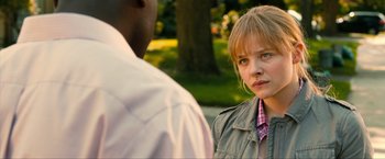 Movie still from “Kick-Ass 2” (2013), directed by Jeff Wadlow – A young woman standing next to a man in a park; Close Up shot, Over the shoulder angle