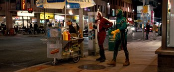 Movie still from “Kick-Ass 2” (2013), directed by Jeff Wadlow – A man in a red suit stands in front of a hot dog cart; Wide shot, High angle