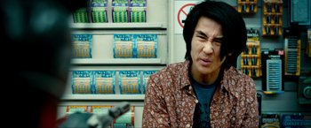 Movie still from “Kick-Ass 2” (2013), directed by Jeff Wadlow – A man in a brown and white shirt in front of shelves of batteries; Close Up shot, Over the shoulder angle