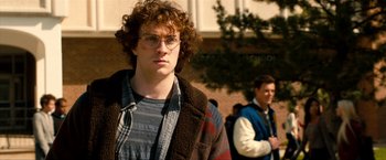 Movie still from “Kick-Ass 2” (2013), directed by Jeff Wadlow – A young man with curly hair wearing glasses and a jacket; Close Up shot, Over the shoulder angle