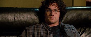 Movie still from “Kick-Ass 2” (2013), directed by Jeff Wadlow – A man with curly hair and glasses sitting on a couch; Close Up shot, Over the shoulder angle