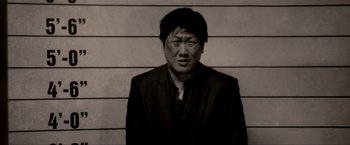 Movie still from “Kick-Ass 2” (2013), directed by Jeff Wadlow – A black and white photo of a man in front of a wall; Close Up shot, Low angle