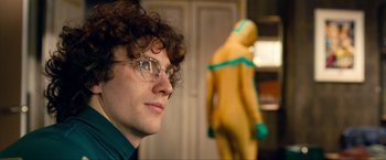 Movie still from “Kick-Ass 2” (2013), directed by Jeff Wadlow – A man with curly brown hair wearing glasses and a green shirt; Close Up shot, Over the shoulder angle