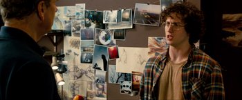 Movie still from “Kick-Ass 2” (2013), directed by Jeff Wadlow – A man standing in front of a bunch of pictures on a wall; Medium shot, Over the shoulder angle