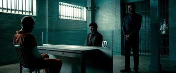Movie still from “Kick-Ass 2” (2013), directed by Jeff Wadlow – A man sitting at a table in a jail cell; Wide shot, Over the shoulder angle