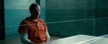 Movie still from “Kick-Ass 2” (2013), directed by Jeff Wadlow – A man in an orange prison uniform sitting in front of a window; Medium shot, Over the shoulder angle