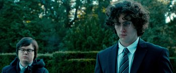 Movie still from “Kick-Ass 2” (2013), directed by Jeff Wadlow – A man in a suit and tie standing in front of a hedge; Close Up shot, Low angle