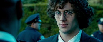 Movie still from “Kick-Ass 2” (2013), directed by Jeff Wadlow – A man with curly hair wearing glasses and a police uniform; Close Up shot, Over the shoulder angle