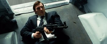 Movie still from “Kick-Ass 2” (2013), directed by Jeff Wadlow – A man sitting on the ground holding a gun; Medium shot, Low angle