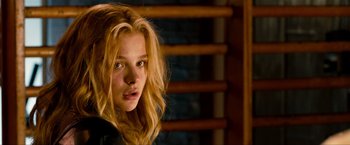 Movie still from “Kick-Ass 2” (2013), directed by Jeff Wadlow – A girl with long blonde hair stares into the camera; Close Up shot, Over the shoulder angle