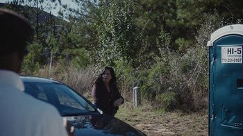 A woman sitting on the hood of a car on the side of the road