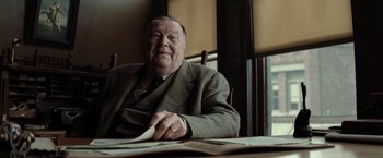 Movie still from “Killers of the Flower Moon” (2023), directed by Martin Scorsese – An older man sitting at a table with papers; Medium shot, Low angle