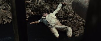 A man laying on the ground next to a rock wall