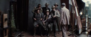 Movie still from “Killers of the Flower Moon” (2023), directed by Martin Scorsese – A group of men sitting on a chair in front of a wall; Wide shot, Low angle