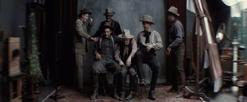 Movie still from “Killers of the Flower Moon” (2023), directed by Martin Scorsese – A group of men sitting on top of a wooden chair; Wide shot, Overhead angle