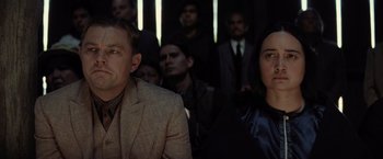 Movie still from “Killers of the Flower Moon” (2023), directed by Martin Scorsese – A man and a woman are standing in front of a group of people; Medium shot, Over the shoulder angle