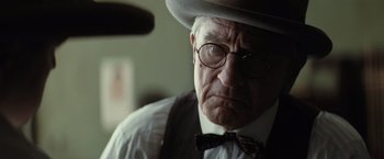 Movie still from “Killers of the Flower Moon” (2023), directed by Martin Scorsese – An older man wearing a hat and glasses; Close Up shot, Over the shoulder angle