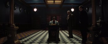 Movie still from “Killers of the Flower Moon” (2023), directed by Martin Scorsese – A man standing in front of a podium in a room; Wide shot, Low angle