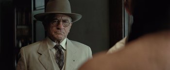 Movie still from “Killers of the Flower Moon” (2023), directed by Martin Scorsese – An older man wearing a hat and glasses; Close Up shot, Over the shoulder angle