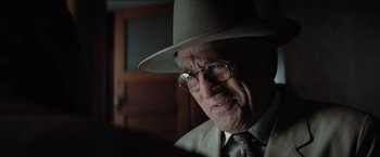 Movie still from “Killers of the Flower Moon” (2023), directed by Martin Scorsese – An older man wearing a hat and glasses; Close Up shot, Over the shoulder angle