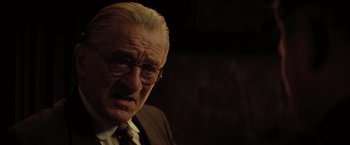 Movie still from “Killers of the Flower Moon” (2023), directed by Martin Scorsese – An older man wearing glasses and a suit; Close Up shot, Over the shoulder angle
