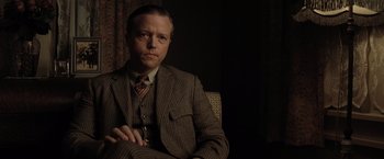 Movie still from “Killers of the Flower Moon” (2023), directed by Martin Scorsese – A man wearing a suit and tie sitting in a chair; Medium shot, Over the shoulder angle