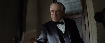 Movie still from “Killers of the Flower Moon” (2023), directed by Martin Scorsese – An older man wearing a suit and tie; Medium shot, Over the shoulder angle