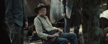 Movie still from “Killers of the Flower Moon” (2023), directed by Martin Scorsese – An old man sitting in a chair holding a gun; Medium shot, Over the shoulder angle