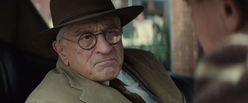 Movie still from “Killers of the Flower Moon” (2023), directed by Martin Scorsese – An older man wearing a hat and glasses; Close Up shot, Over the shoulder angle