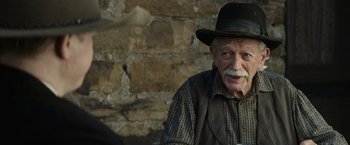 Movie still from “Killers of the Flower Moon” (2023), directed by Martin Scorsese – An old man wearing a black hat and vest; Close Up shot, Over the shoulder angle