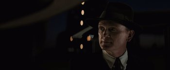 Movie still from “Killers of the Flower Moon” (2023), directed by Martin Scorsese – A man wearing a suit and a hat in the dark; Close Up shot, Over the shoulder angle